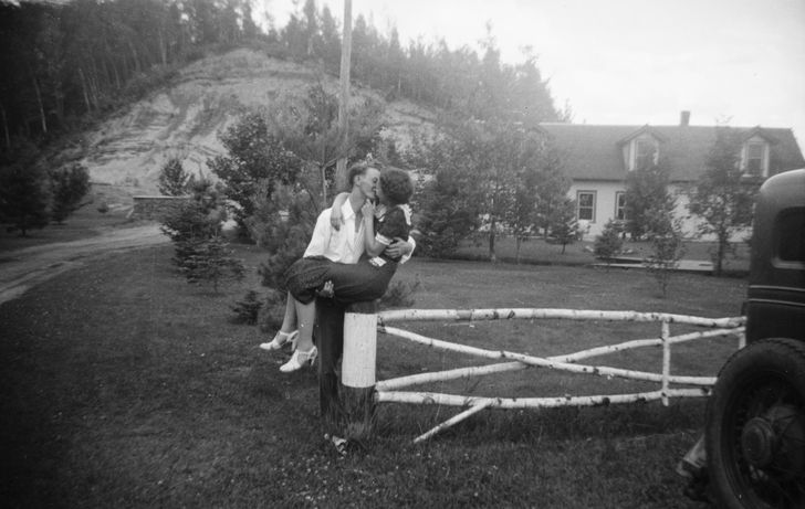 couple kissing while sitting on a fence