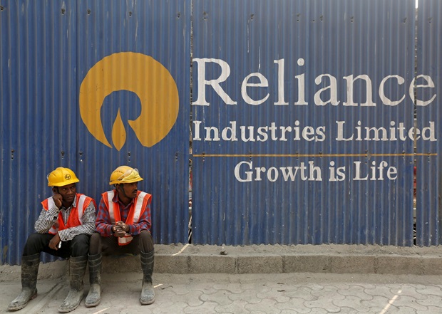 Labourers rest in front of an advertisement of Reliance Industries Limited at a reliance construction site in Mumbai
